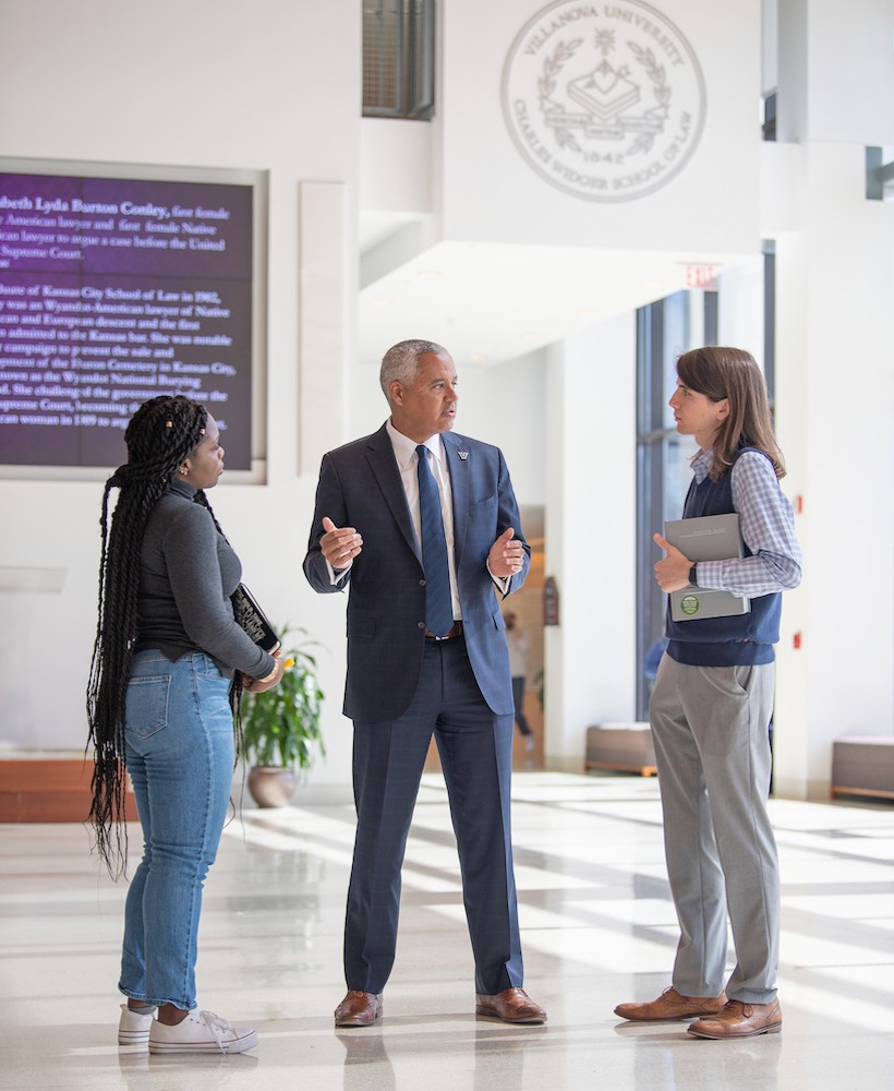 Mark Alexander, Dean of Villanova's Law School, stands in the Law School Commons talking with two students.