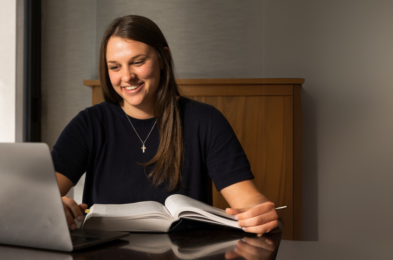 female student reading a textbook in front of her laptop