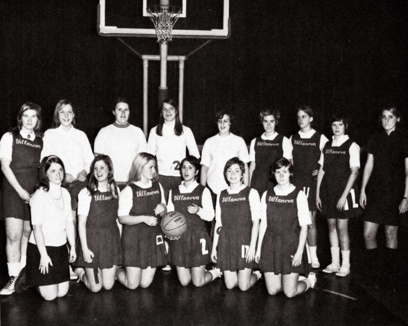Black and white team photo of Villanova Women’s Basketball in their first uniform, a jumper dress embroidered with Villanova 