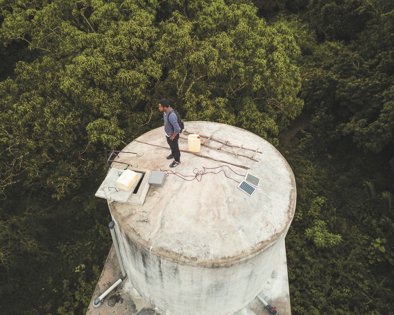 Surrounded by trees, Malagasy CRS partner stands atop a water tower where he installed remote-sensing technology