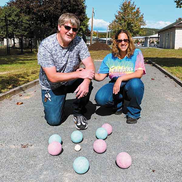 two Special Olympics participants, one male, one female, kneel on asphalt while holding hands and smiling
