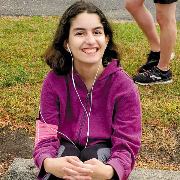smiling female athlete wearing earbuds sitting on a concrete parking block