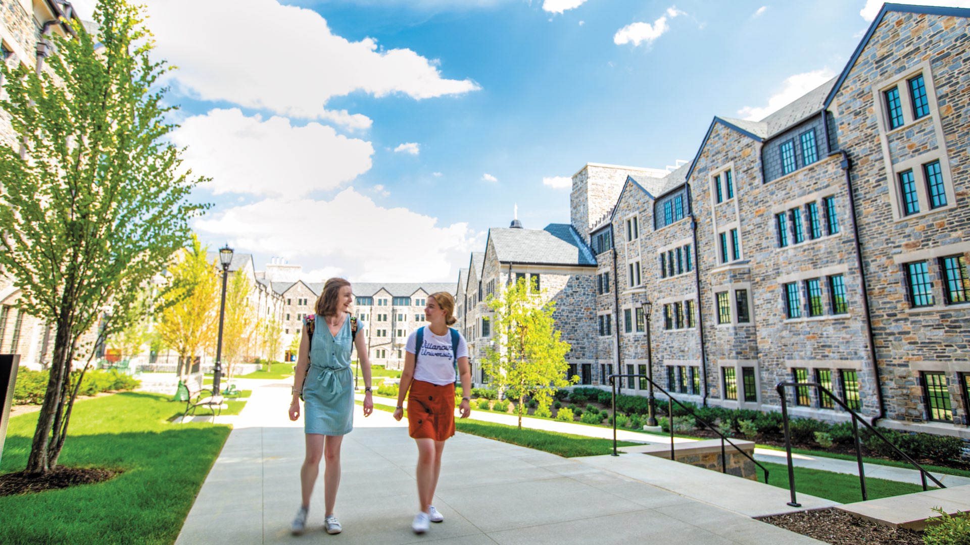 Two female students in backpacks walking through The Commons on a bright sunny day