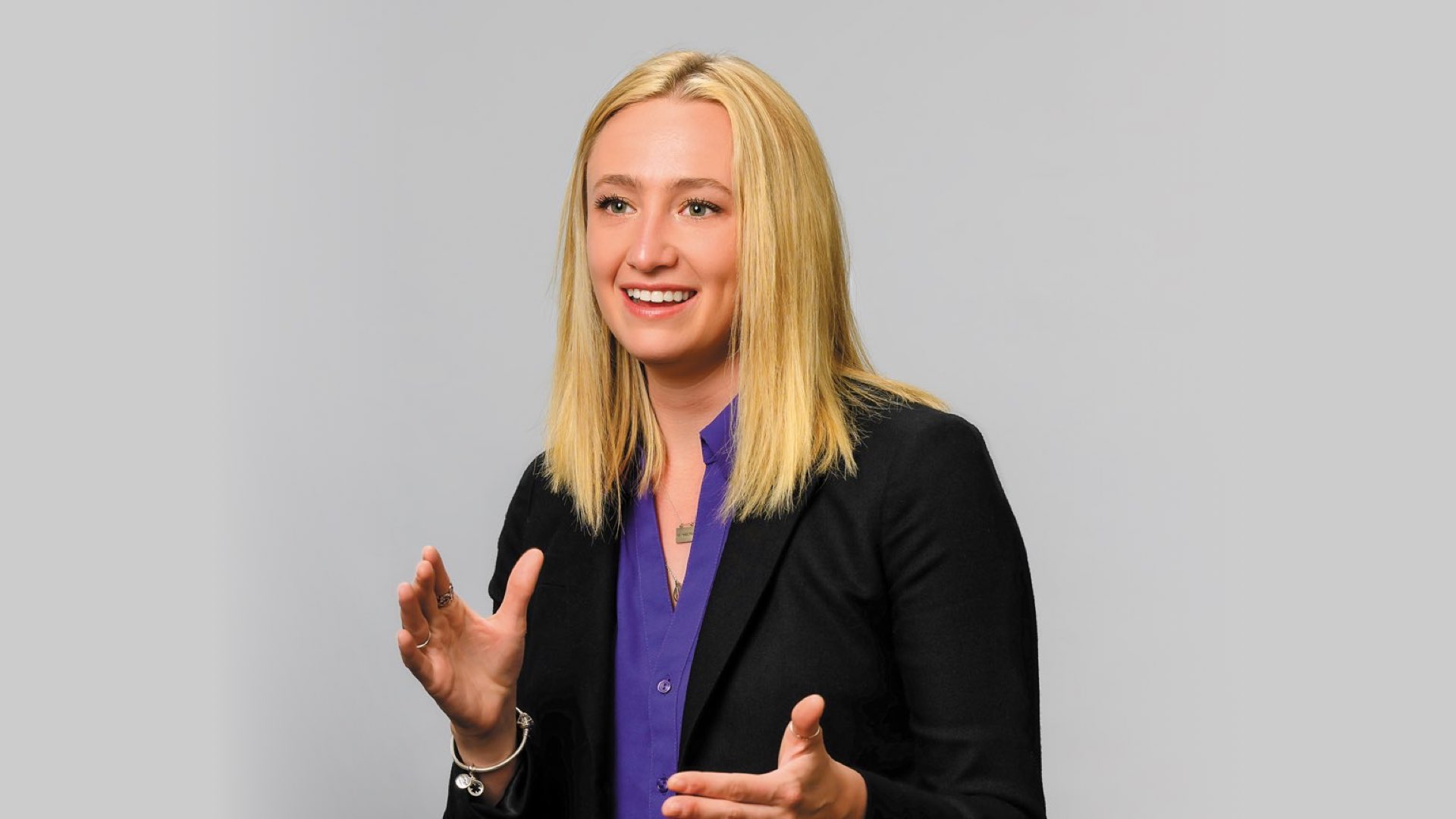 Talking with her hands, recent CLAS graduate MK Smith is wearing a blazer with jeans and a purple shirt