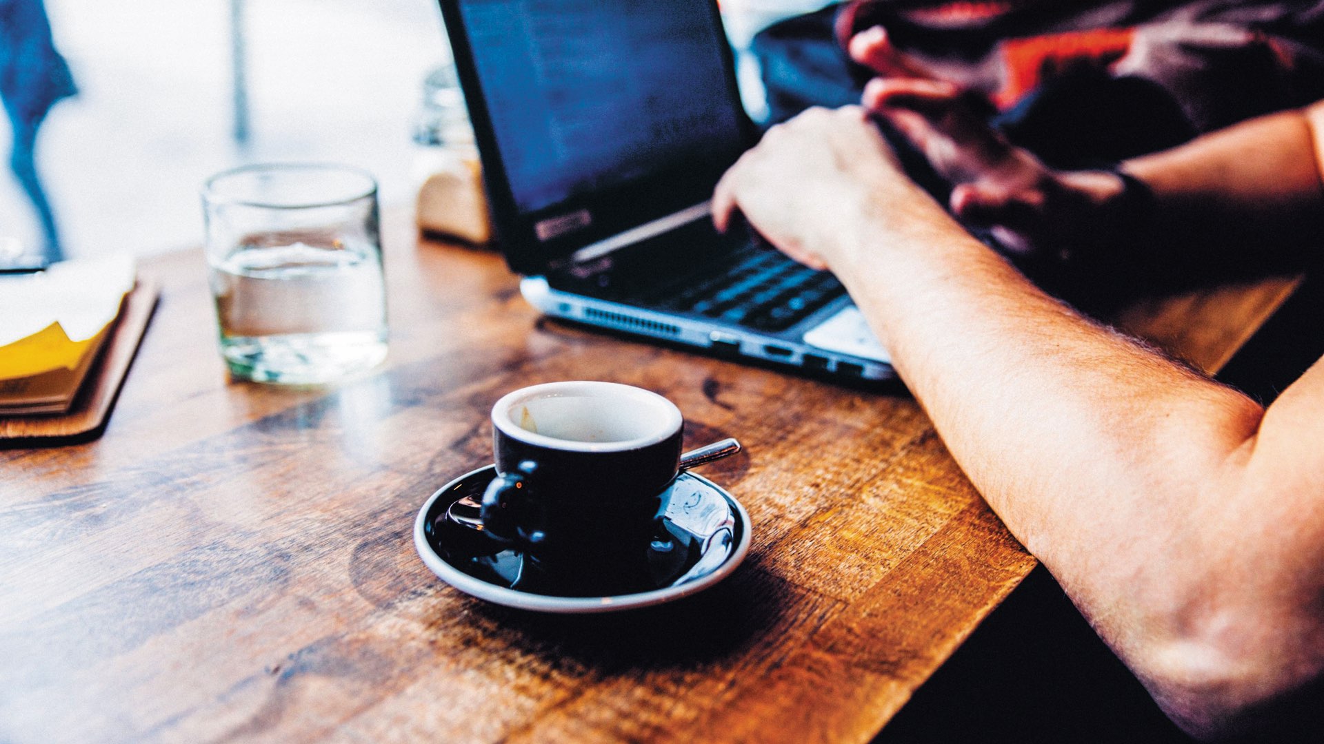 Close-up of hands typing on a laptop at a coffee bar with a cup of espresso on the table