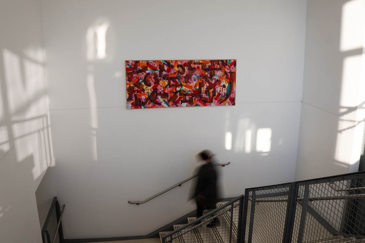 CPX391_20220201_172_wsplit A person walking down the stairs with a piece of art on the wall behind them