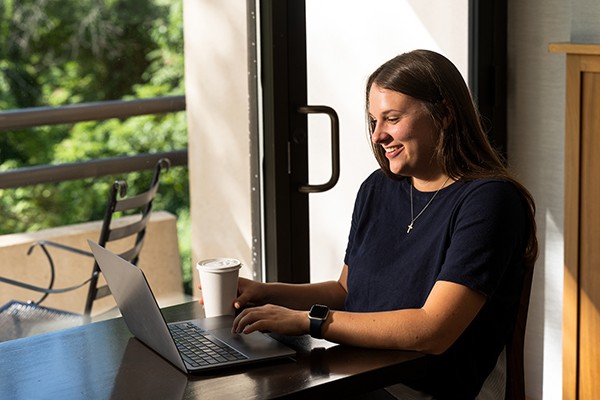 student sitting in windowsill looking at laptop