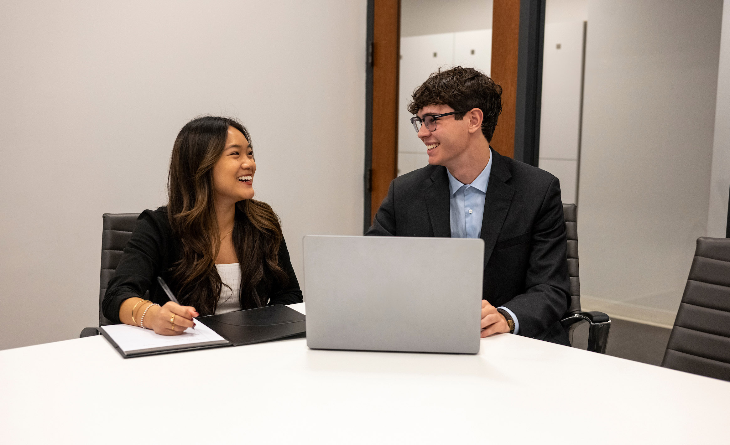 Two students in sitting at a table in a conference room.