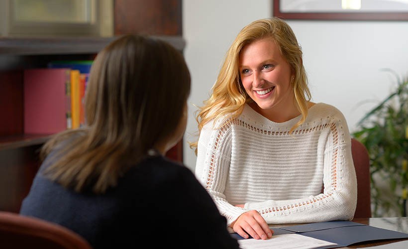 An advisor and a student sit together at a table.