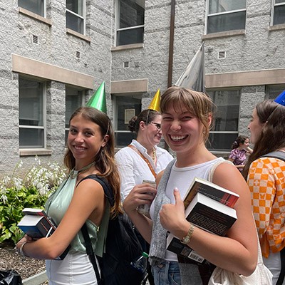 Humanities alumni holding books outside and wearing party hats. Humanities alumni holding books outside and wearing party hats.