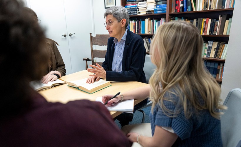 Professor leads a group discussion with students sitting at a table.