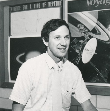 Dr. Guinan sits in front of his research team's poster displaying evidence for a ring around Neptune in 1982. A poster of the Voyager missions hangs adjacent, foreshadowing Voyager 2's photographic confirmation of the the planet's ring system in 1989. Dr. Guinan sits in front of his research team's poster displaying evidence for a ring around Neptune in 1982. A poster of the Voyager missions hangs adjacent, foreshadowing Voyager 2's photographic confirmation of the the planet's ring system in 1989.
