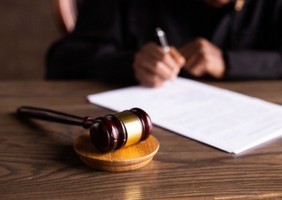 A judge signs a court paper, with a gavel on the desk nearby