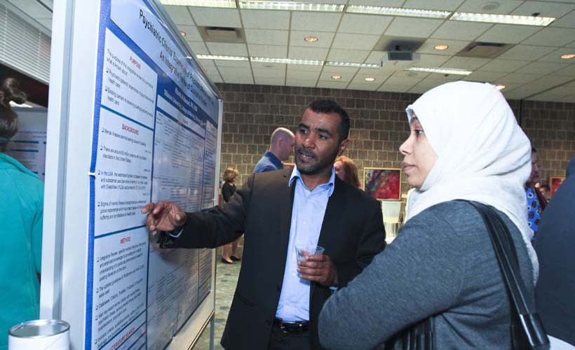 Male PhD student<br/> xplains his research poster.