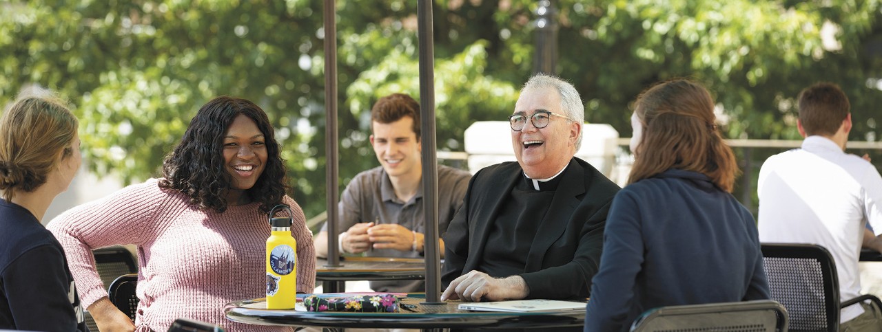 Father Peter laughing with students Father Peter seated outside laughing with students