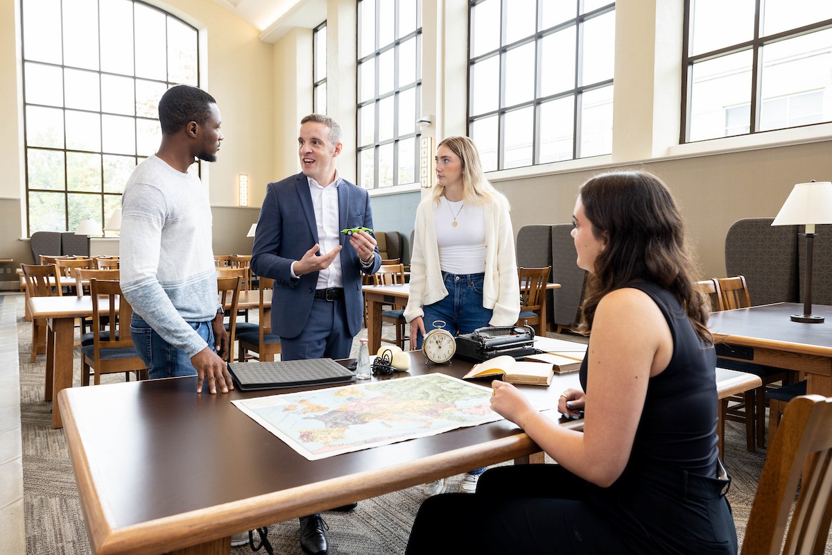Students listening to a professor talk over a table