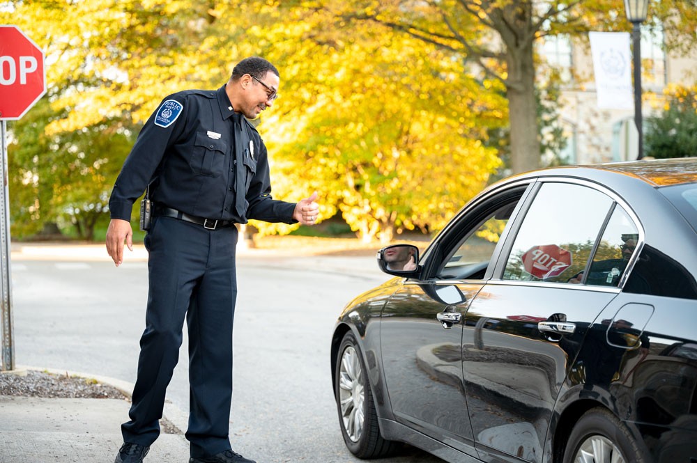 A male public safety officer in uniform greets a vehicle.