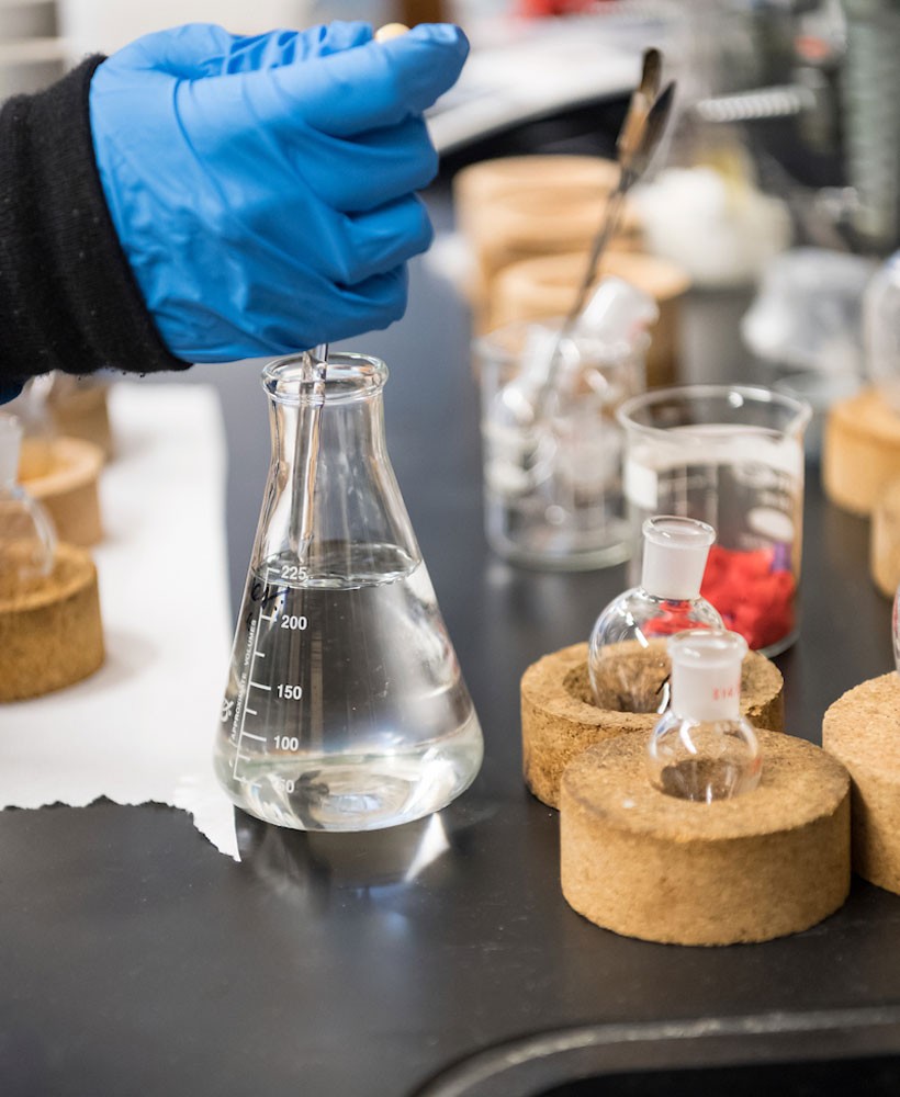 Hand dripping liquid into container in a lab