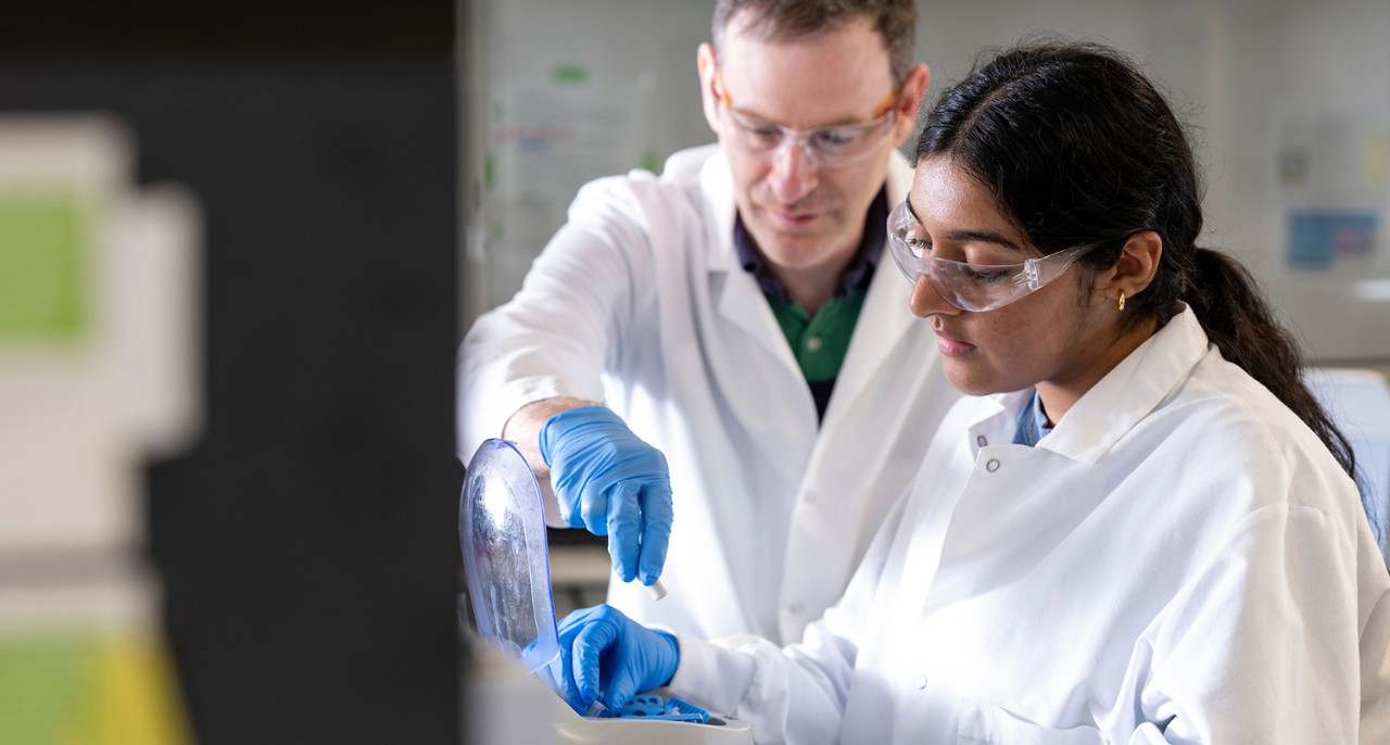 student and faculty working in lab wearing white lab coats and gloves