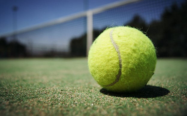 Clos up of green tennis ball on green tennis court 