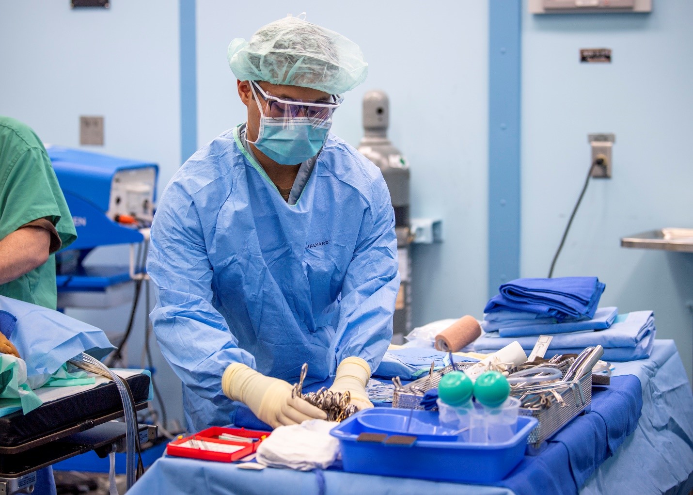 Surgeon in surgical gown and cap standing before a table of medical instruments preparing them for surgery