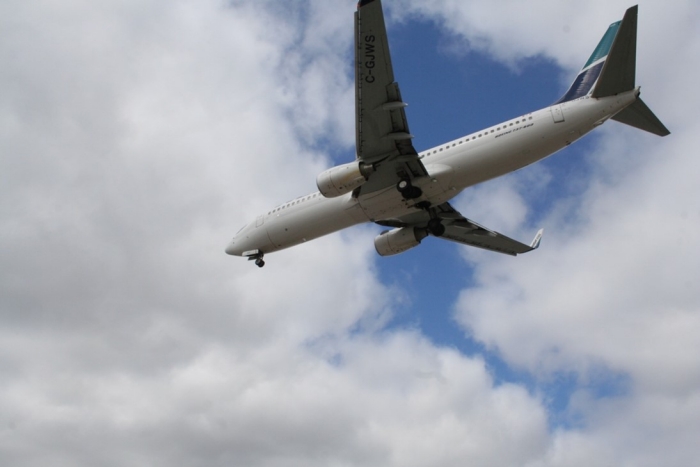 Airplanes photo showing underside of a passenger jet passing through a blue sky with white clouds