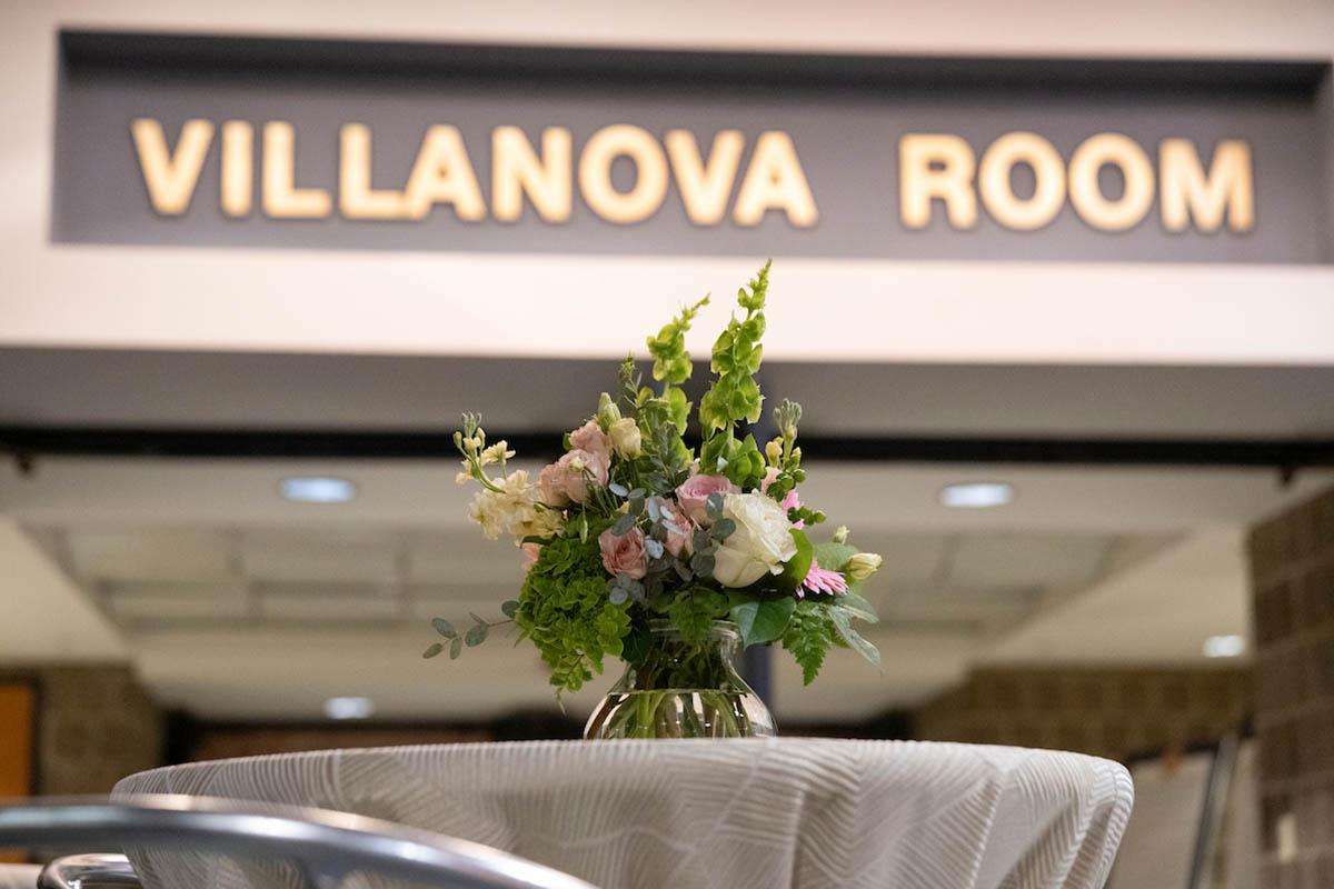 A vase of flowers in front of a sign reading "Villanova Room"