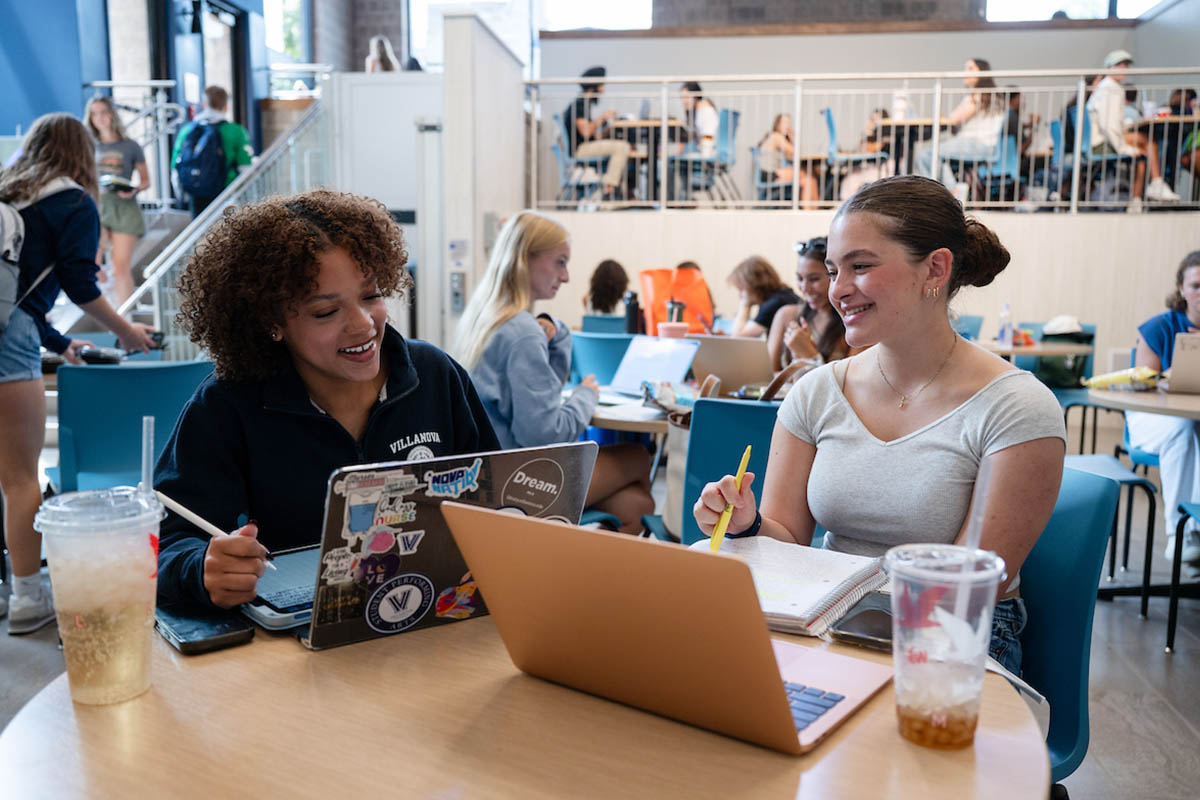 Two students sitting at a table with laptop and work supplies