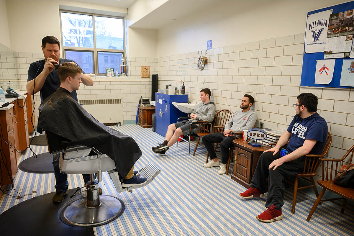 Students sitting in a barbershop while a barber cuts someone's hair