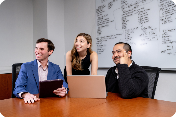 Three students smiling in front of laptop