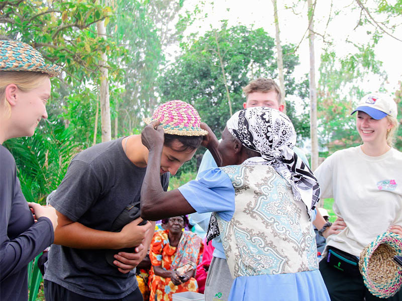 A woman in Kenya placing a hat on a student