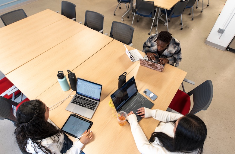 A bird's eye view of three students working at a table with laptops