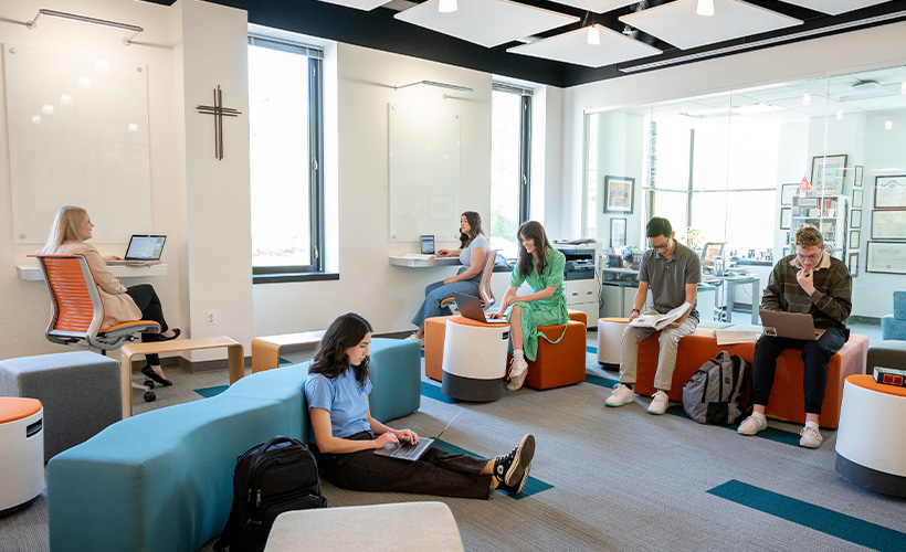 group of students sitting in a room; some are studying, some are on their laptops, some are conversing