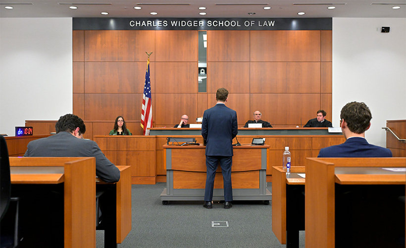 student standing in courtroom classroom in front of a panel of judges