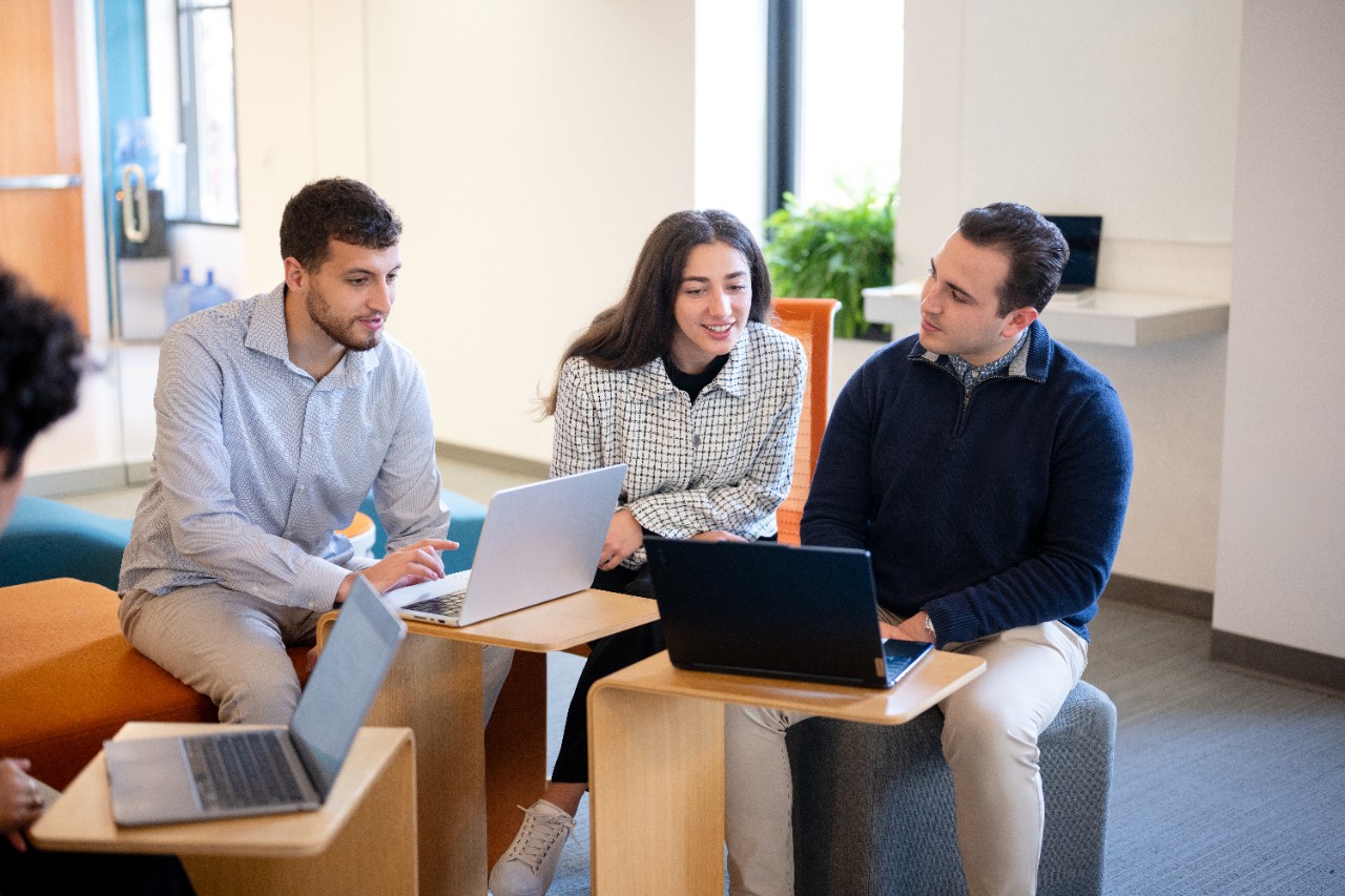 Three students sit around laptops in an academic classroom