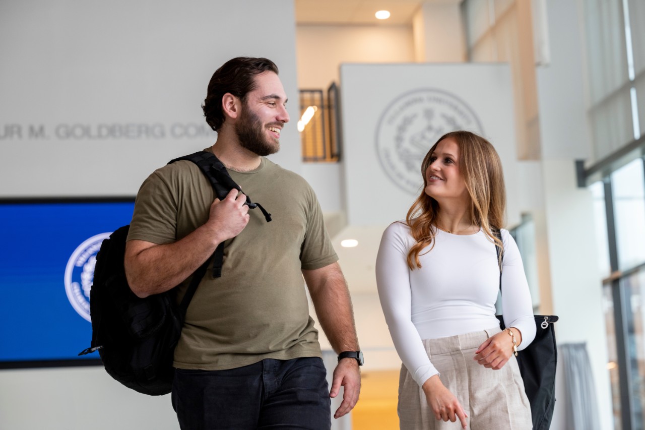 Two students in conversation walk with backpacks on their shoulders.