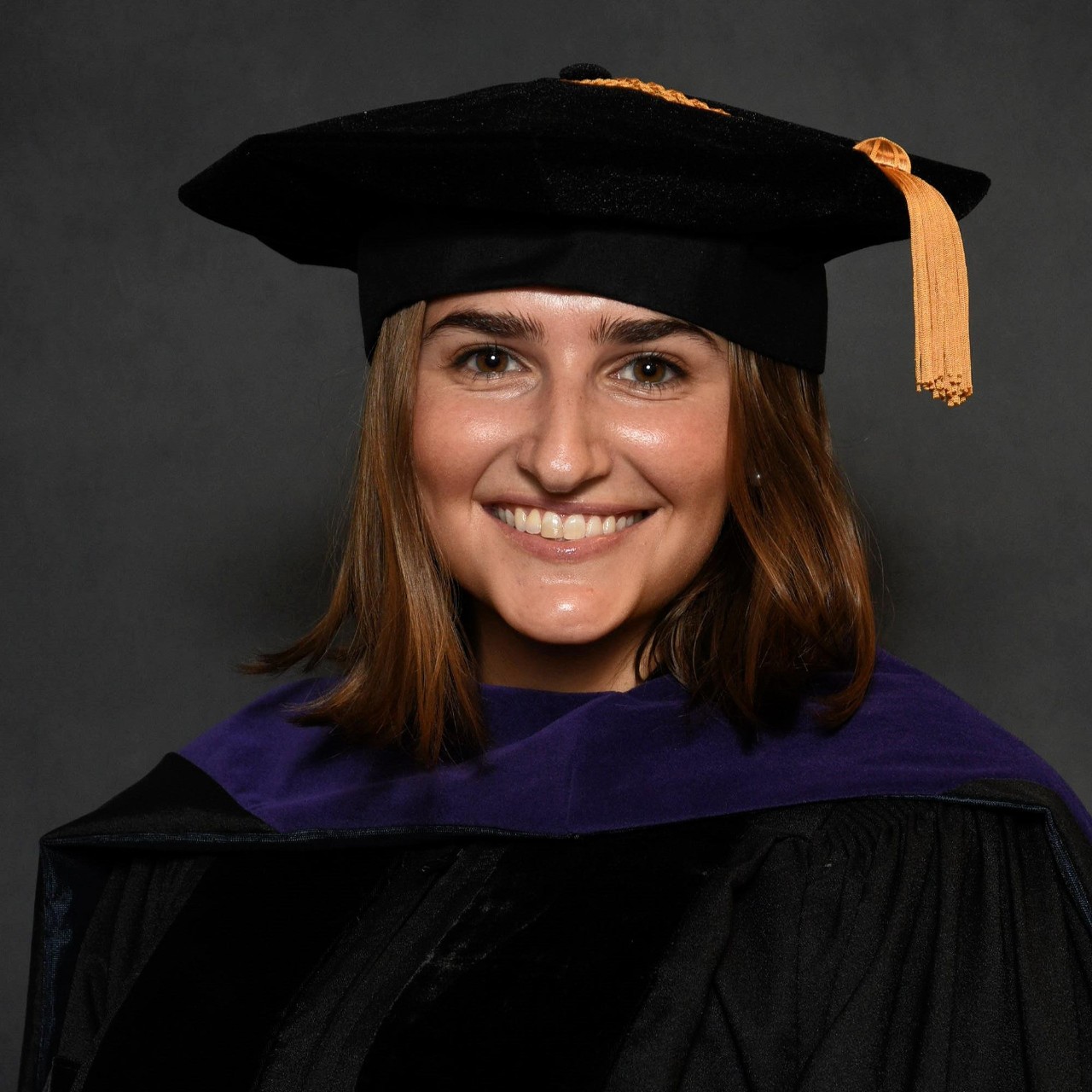 Headshot of a woman in a graduation cap against a dark background