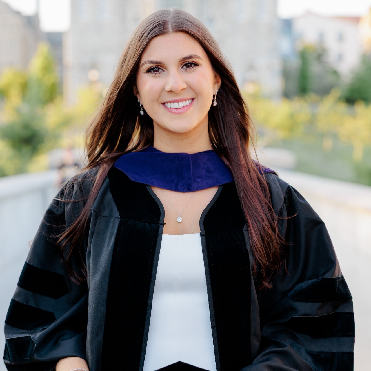  Image of a woman in a graduation gown standing in front of a blurred background of a building