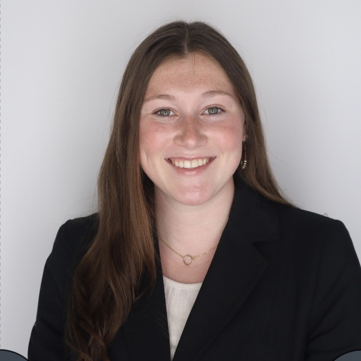  Headshot of a woman in a black blazer against a light gray background