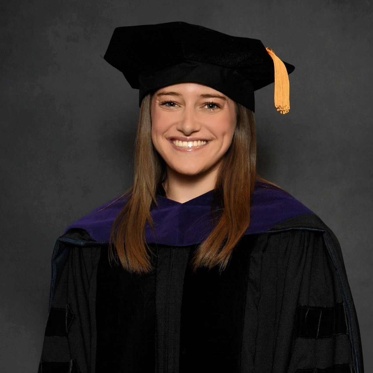  Headshot of a woman in a graduation cap and gown against a gray background