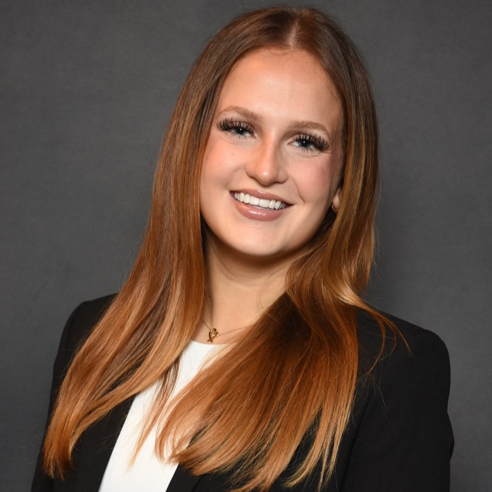  Headshot of a woman in a black blazer against a gray background
