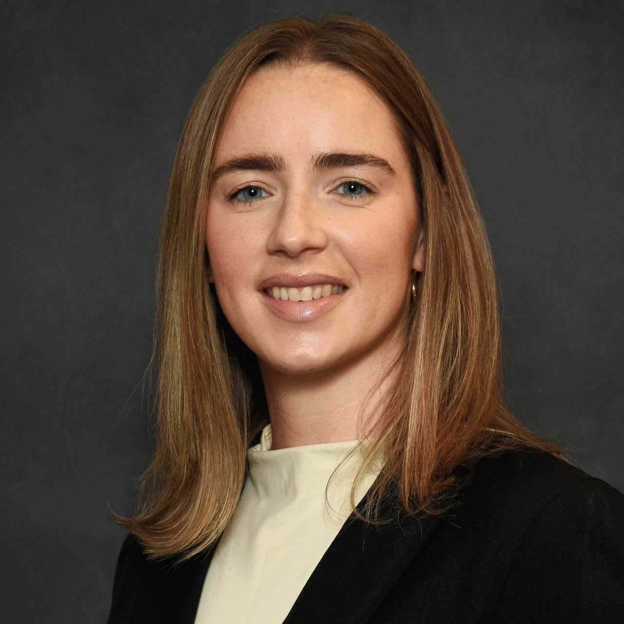 Headshot of a woman in a black blazer against a gray background