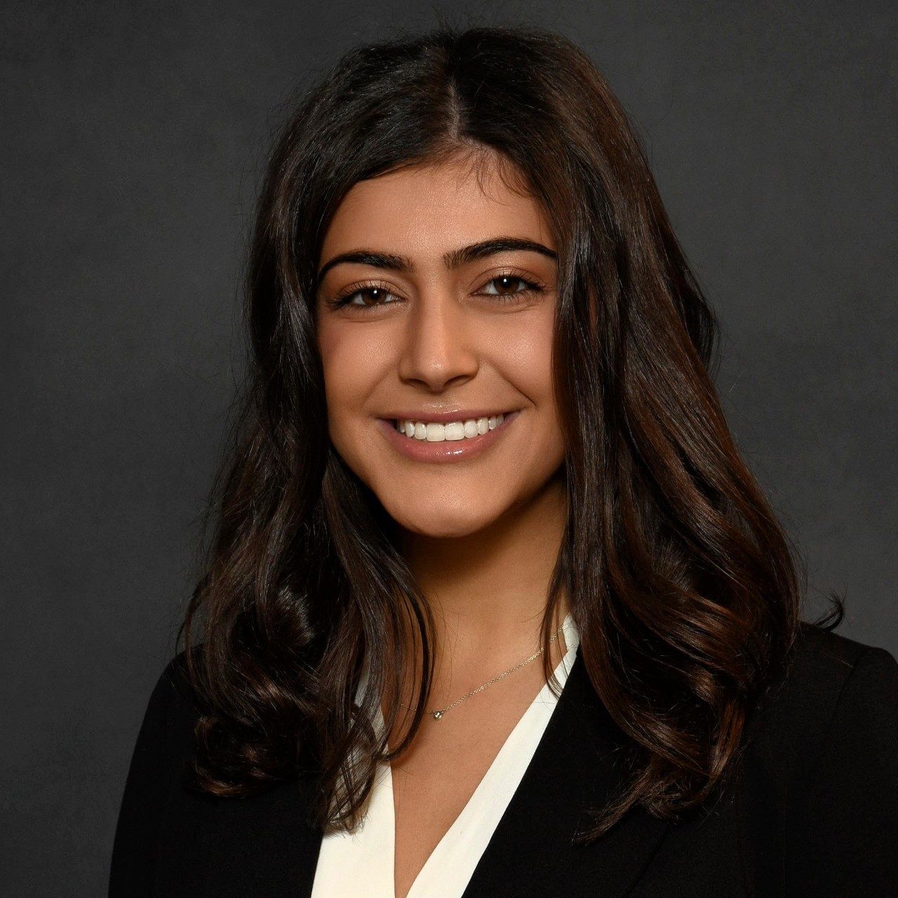  Headshot of a woman in a black blazer against a gray background