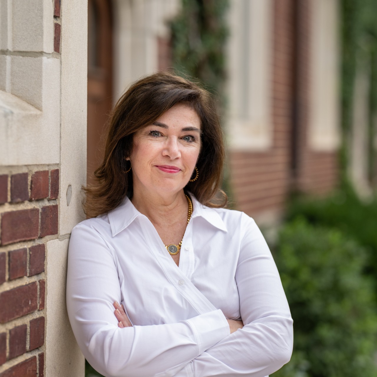A woman in a white blouse leans against a brick wall.