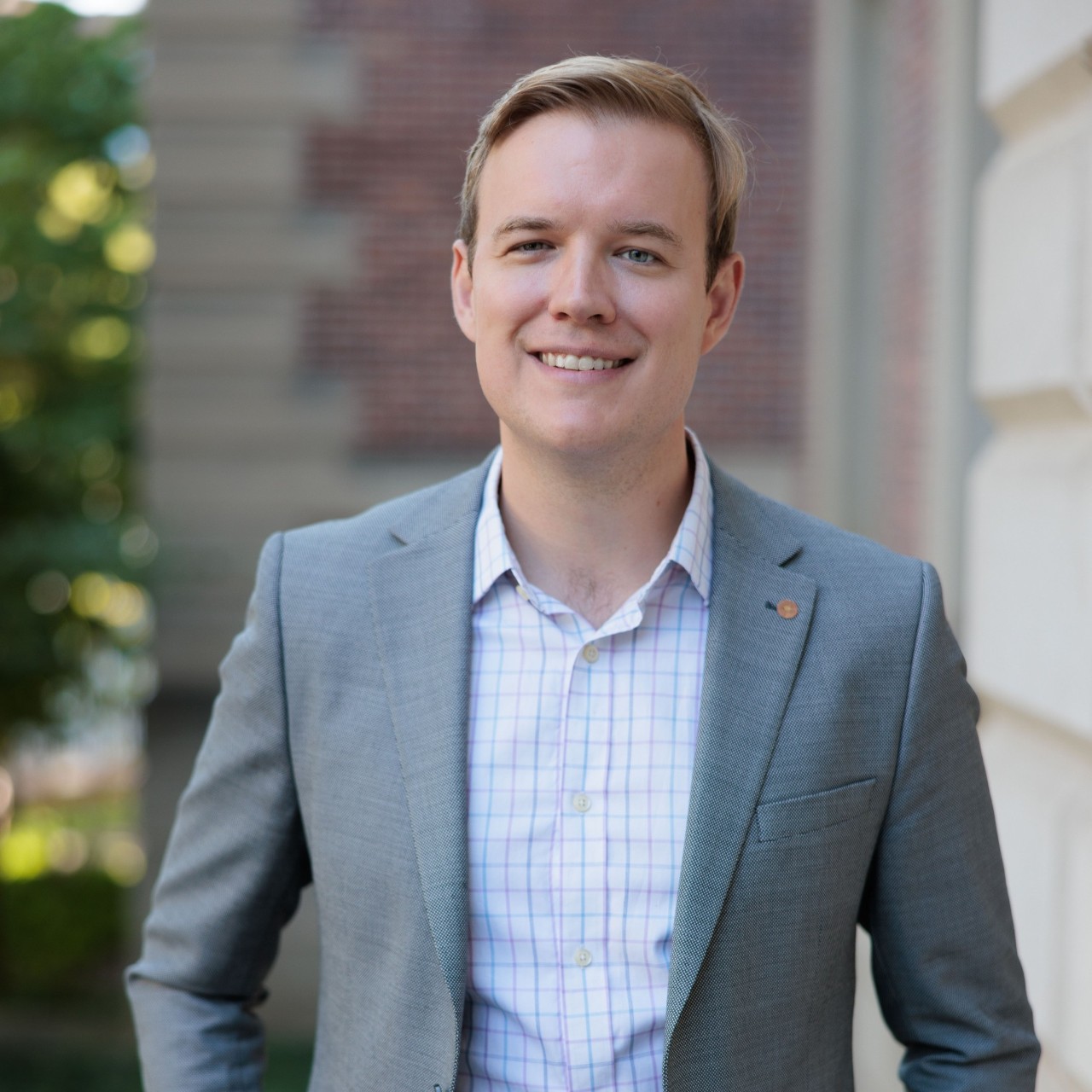 A man in a suit smiles in front of a brick building.