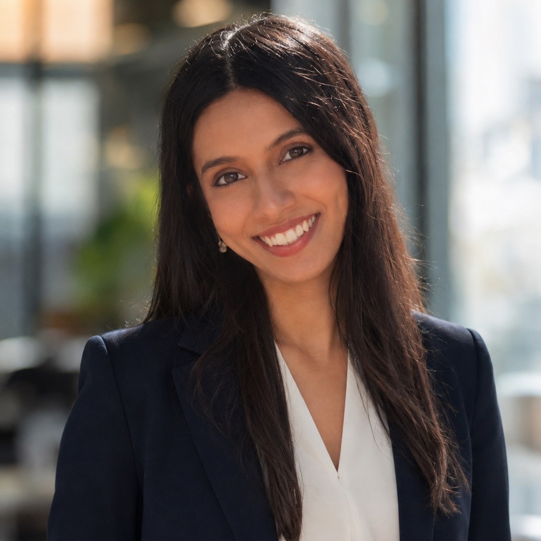 Headshot of a woman wearing a black blazer and white blouse smiling in front of a blurred background