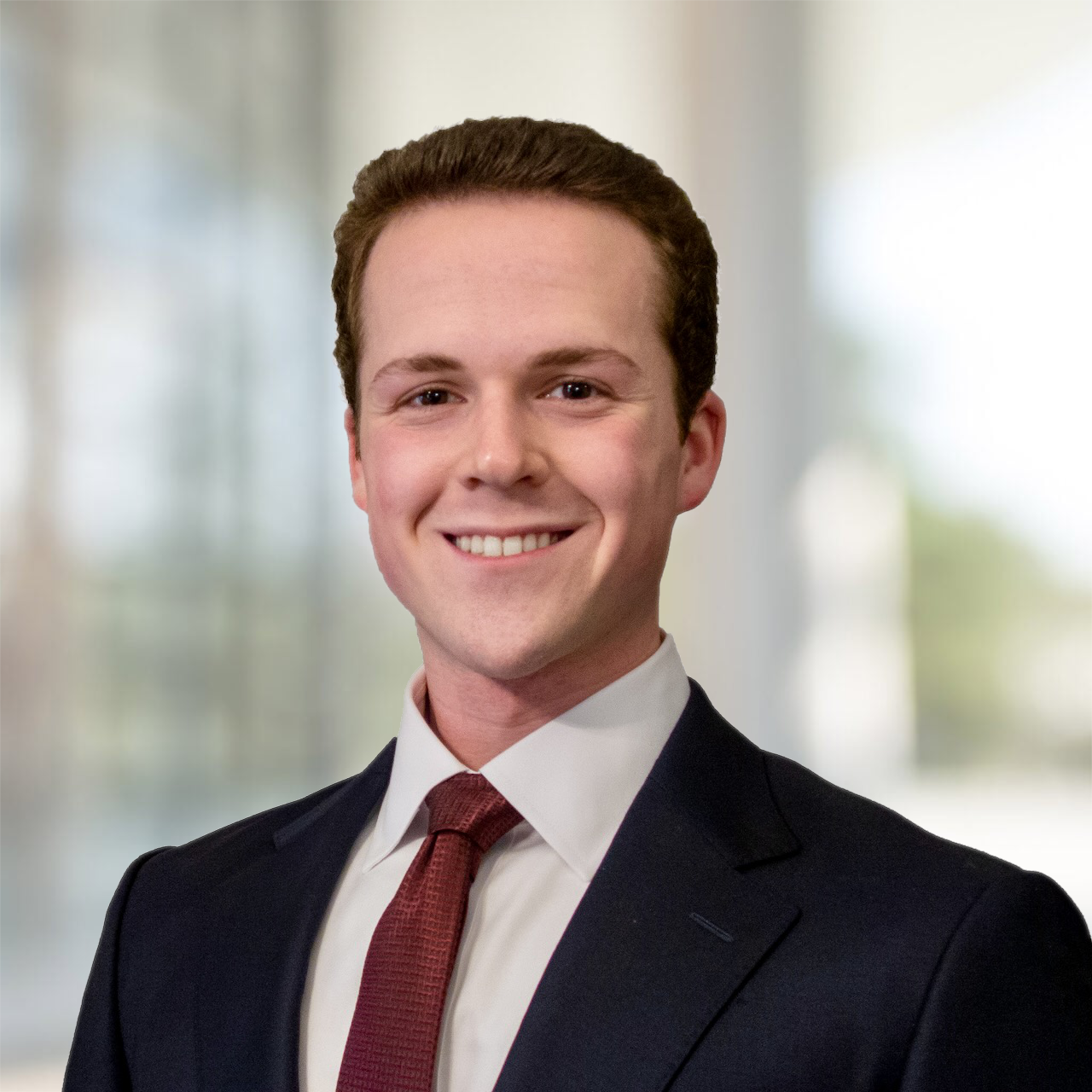 Headshot of a man wearing a suit and tie, smiling in front of a blurred background