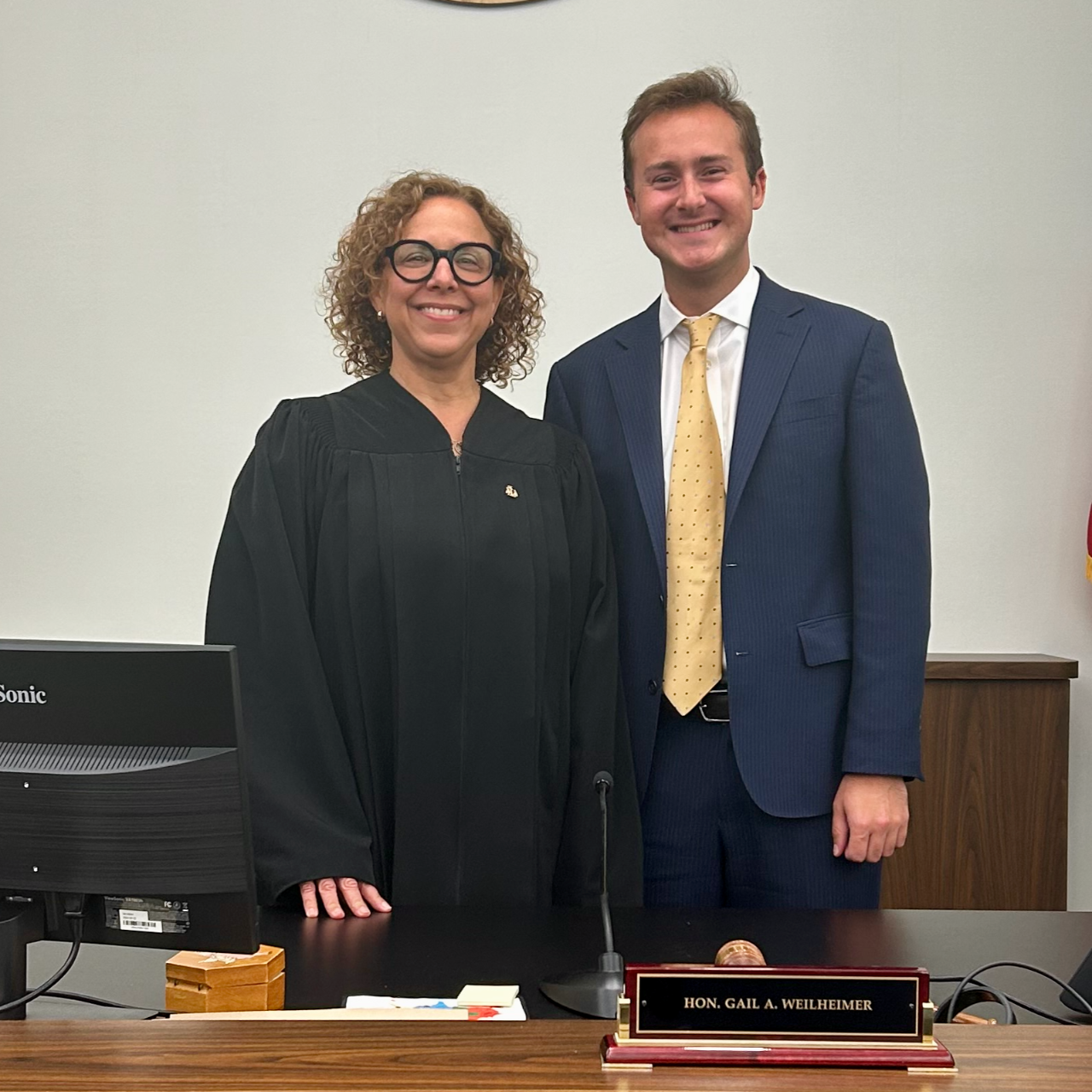 Photo of a court judge wearing official robes standing next to a man in a blue suit, standing in an office behind a desk
