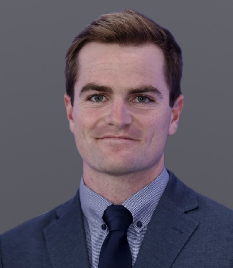Headshot of a man in a navy blazer standing in front of a dark gray background