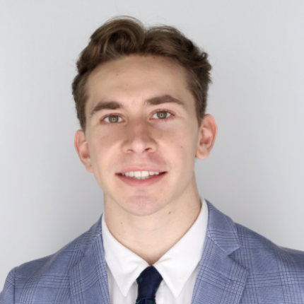 Headshot of a man wearing a light gray suit jacket in front of a light gray background